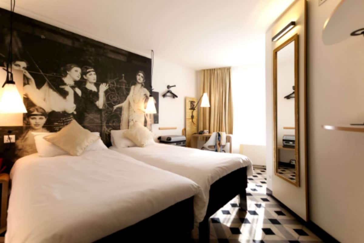 A hotel room with two beds, a large mirror, a wall with a poster, and a checkered floor.