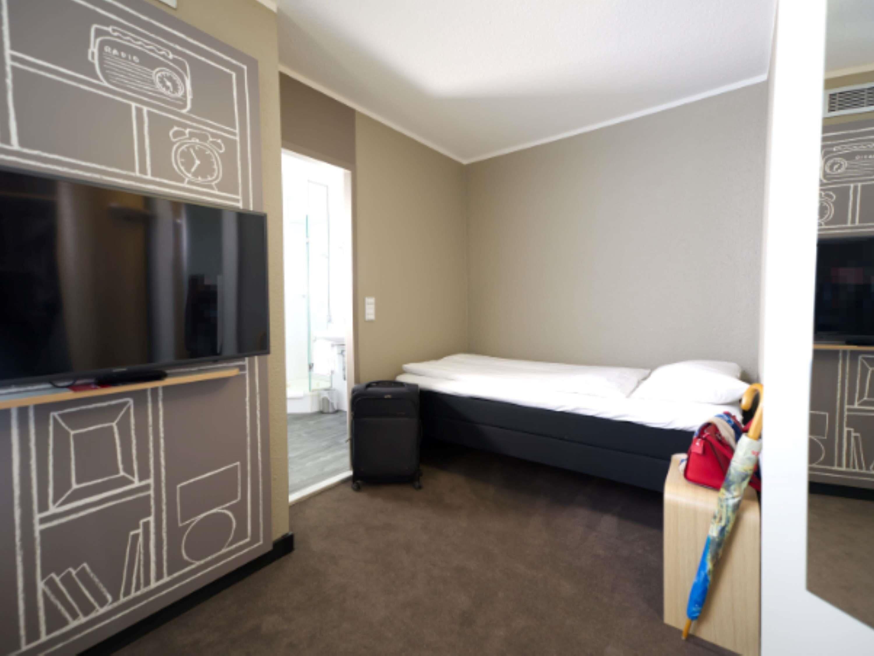 A hotel room with a bed, a television, a suitcase, and a wall with a geometric pattern.