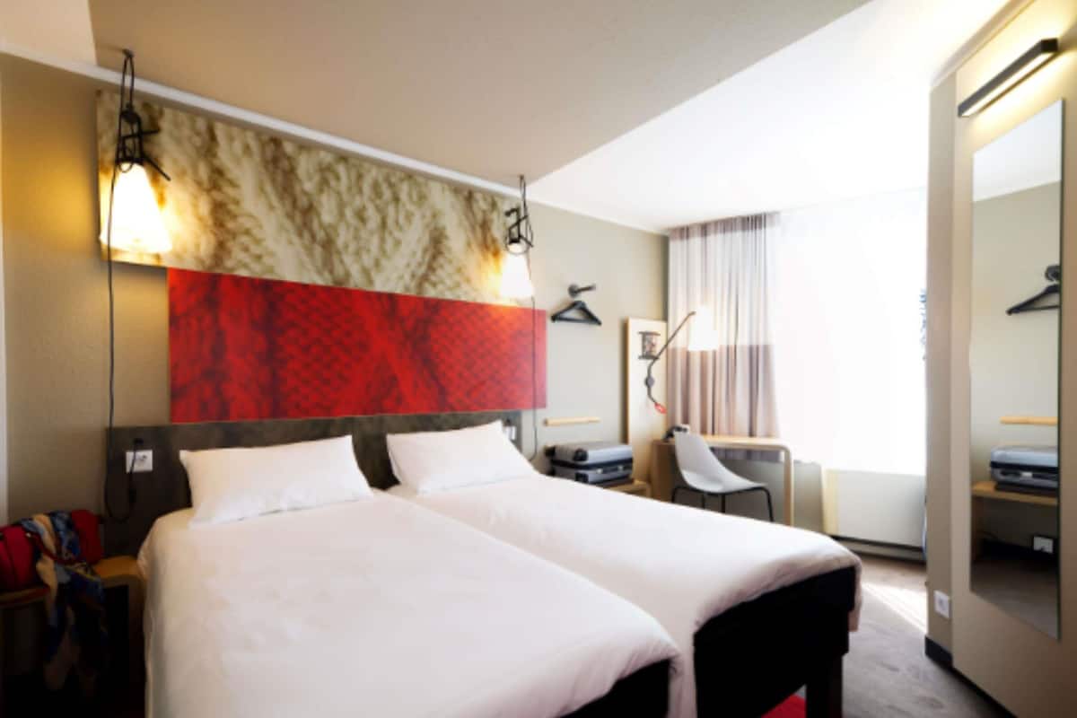 A hotel room with a large bed, a desk, a chair, a wardrobe, and a mirror.