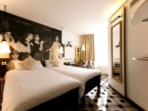 Une chambre d’hôtel avec deux lits, un grand miroir, un tableau au mur et un comptoir d’enregistrement.