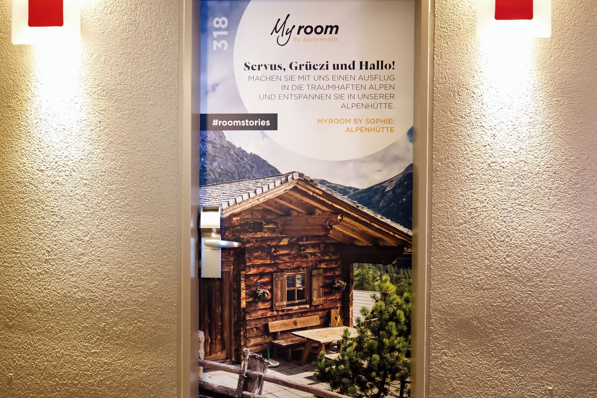 A hotel entrance with a poster advertising a room featuring a mountain view, a wooden cabin, and a sign with the number 318.