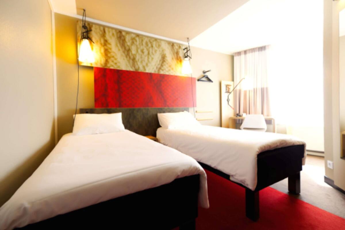 A hotel room with two beds, a red carpet, and a large window with curtains.