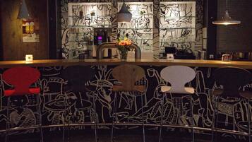 A bar area with graffiti-style wall art, a counter with a coffee machine, and metal chairs with unique designs.