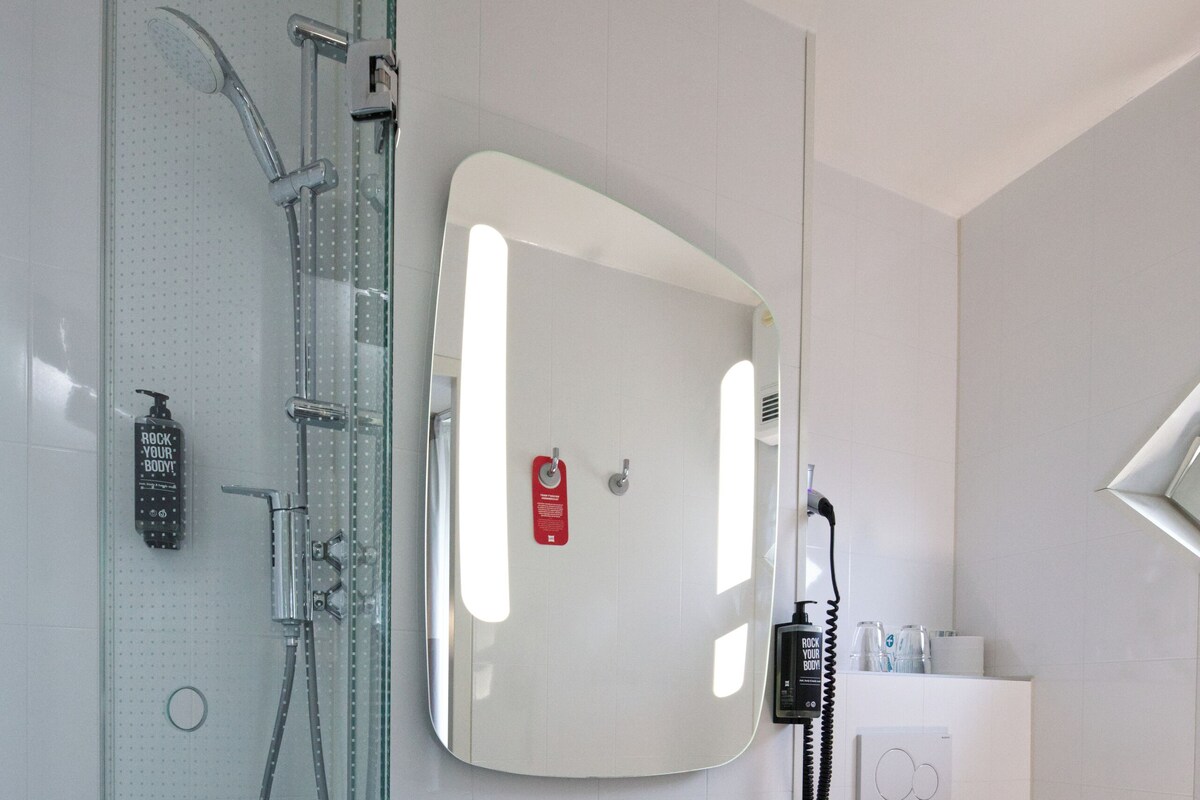 A modern bathroom with a glass shower enclosure, a white sink, a mirror, and a toilet.