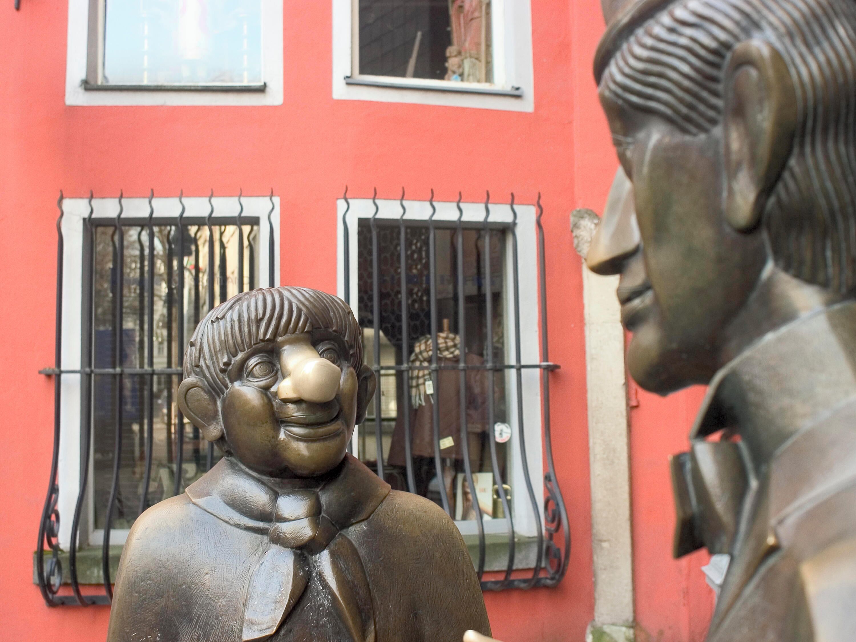 Une statue d’un homme portant un nœud papillon, devant un bâtiment aux fenêtres grillagées.