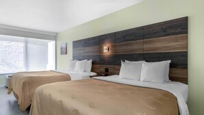 A hotel room with two beds, beige bedding, a wooden headboard, a nightstand, and a wall-mounted light. - Quality Inn University North I-75 (Gainesville)