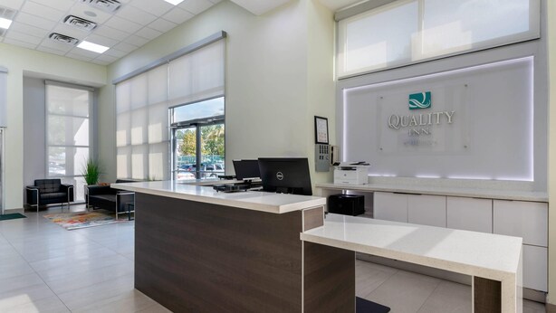 A modern reception desk with a computer, a large window, and a sign for Quality Inn. - Quality Inn University North I-75 (Gainesville)
