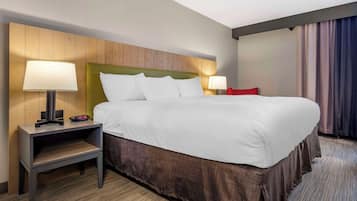 Habitación de hotel con una cama grande, dos mesitas de noche con lámparas, un cabecero de madera y vistas al exterior a través de cortinas.