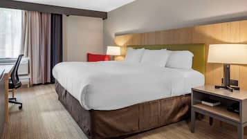 A hotel room with a large bed, a desk with a chair, a lamp, and a window with curtains.