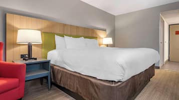 Une chambre d’hôtel avec un grand lit, deux lampes de chevet, un fauteuil rouge et une tête de lit en bois.