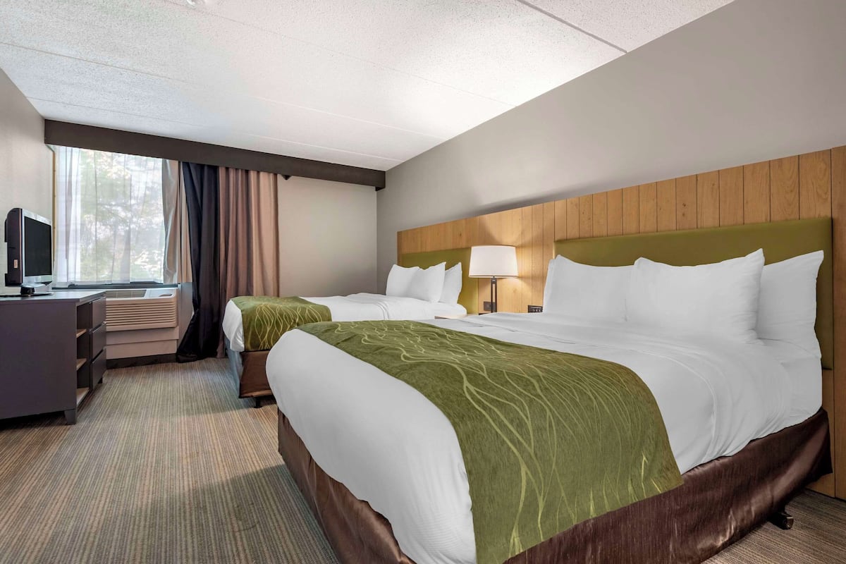 A hotel room with two beds, a desk with a computer, and a window with curtains.