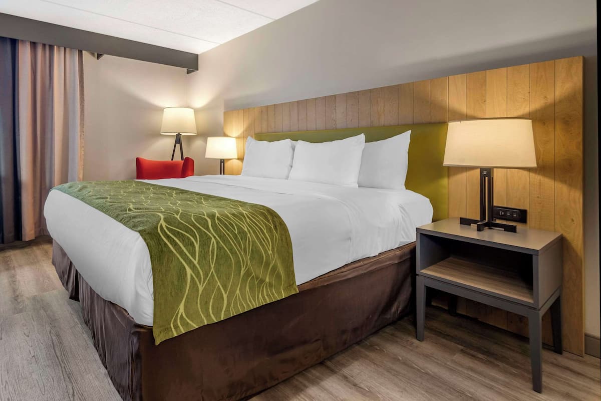 A hotel room with a large bed, two bedside lamps, a wooden headboard, and a small nightstand.