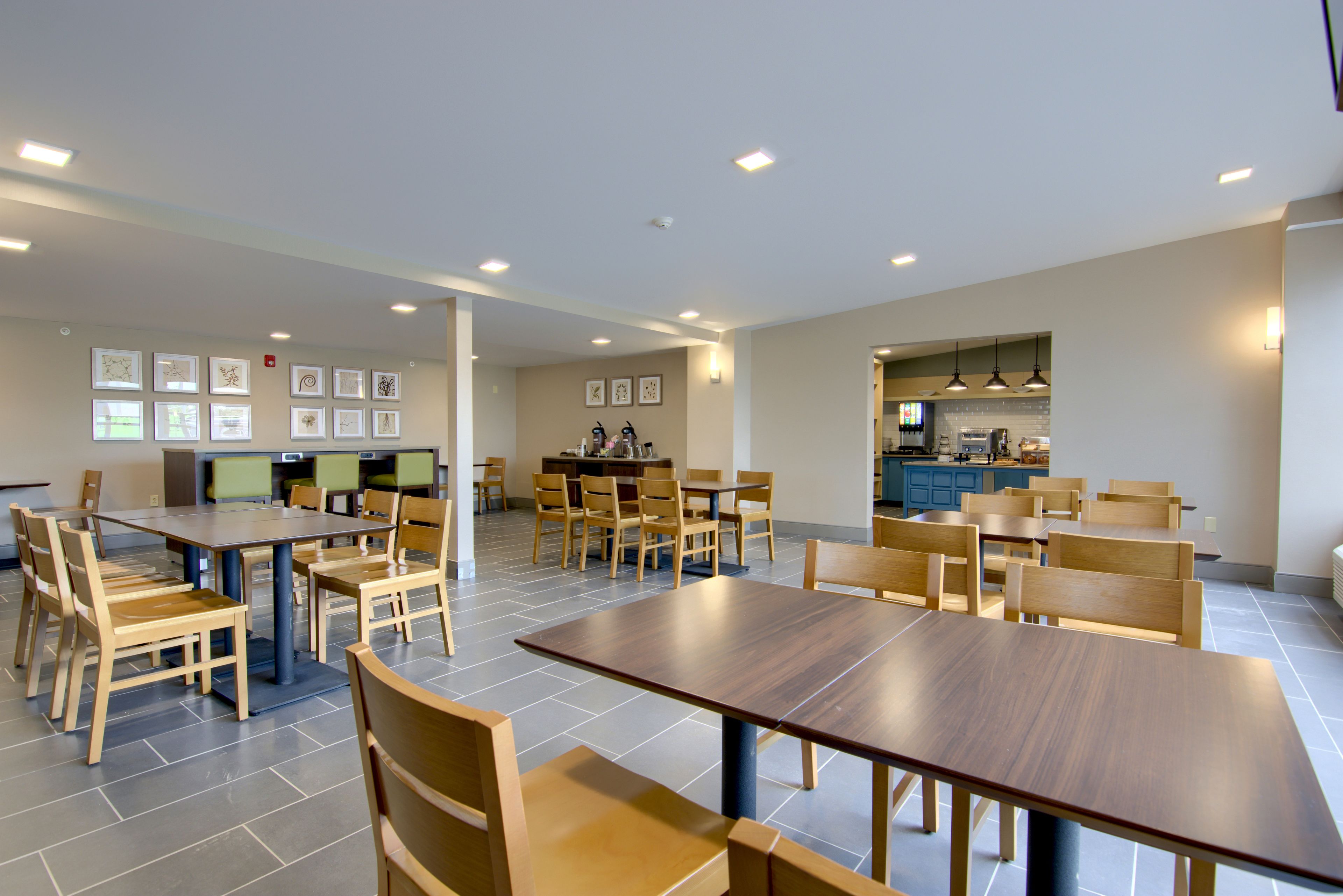 Un grand espace à manger avec de nombreuses tables et chaises en bois, une cuisine à l’arrière-plan et des œuvres d’art encadrées accrochées aux murs.