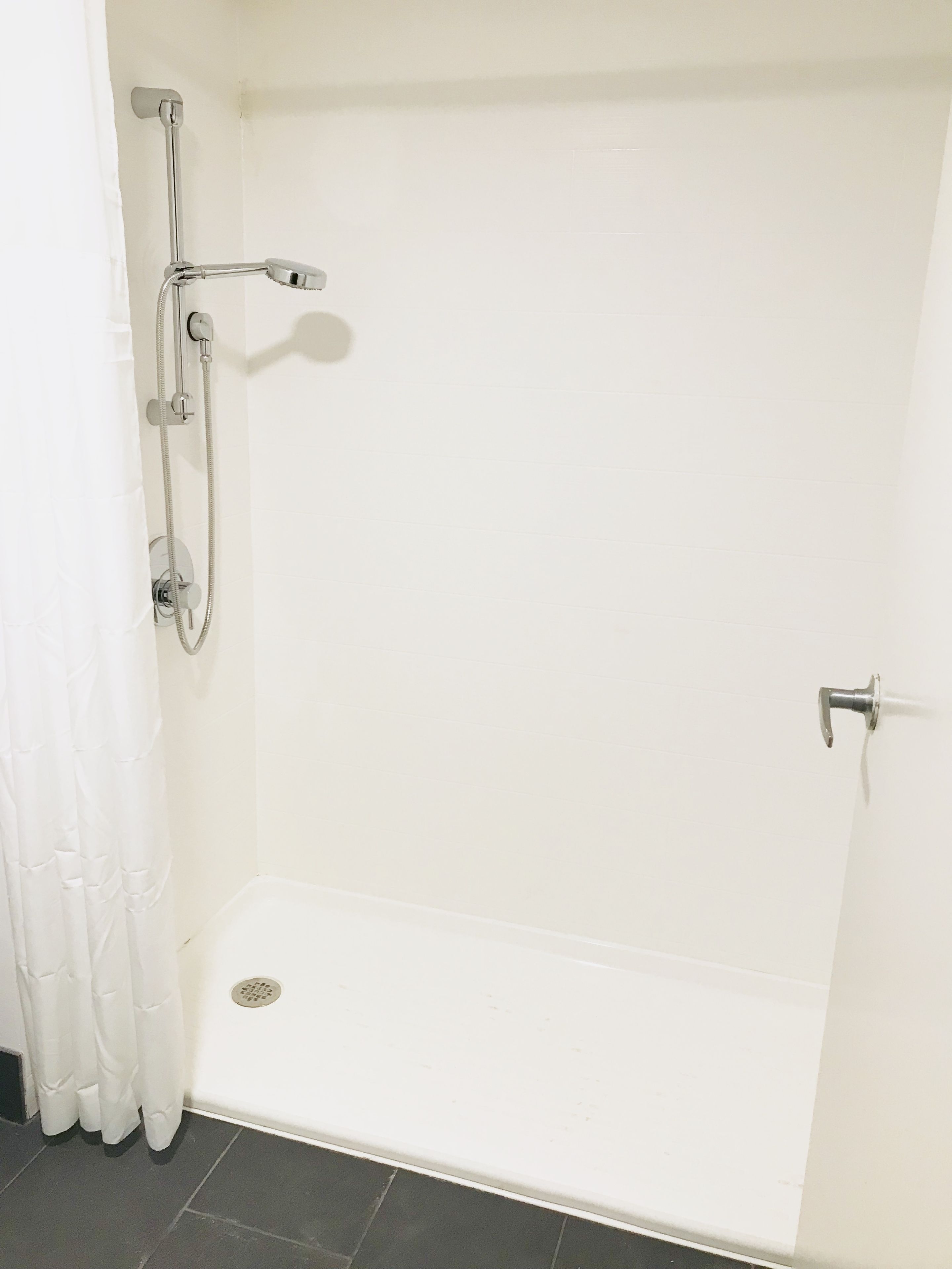 A walk-in shower with a white tiled wall, a showerhead, and a handheld shower attachment.