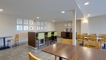 A modern dining area with wooden tables and chairs, a counter with stools, and framed artwork on the walls.