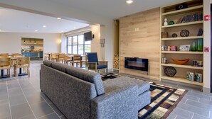 A modern living room with a grey sofa, wooden chairs, a bookshelf, and a TV.