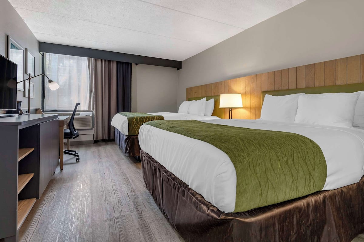 A hotel room with two beds, a desk, a chair, a TV, and a window with curtains.