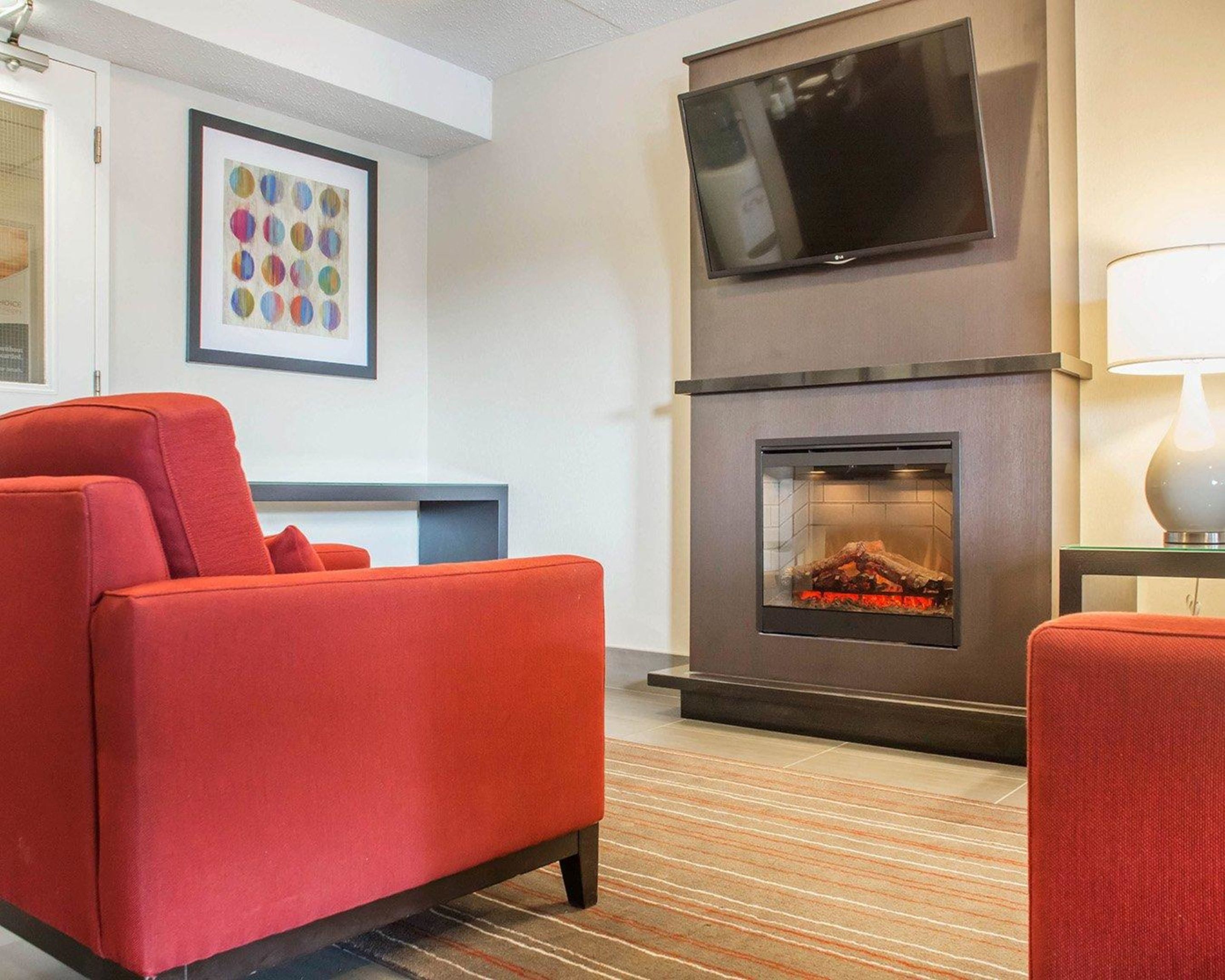 A modern living room with a red sofa, a flat-screen TV mounted above a fireplace, and a framed artwork on the wall.