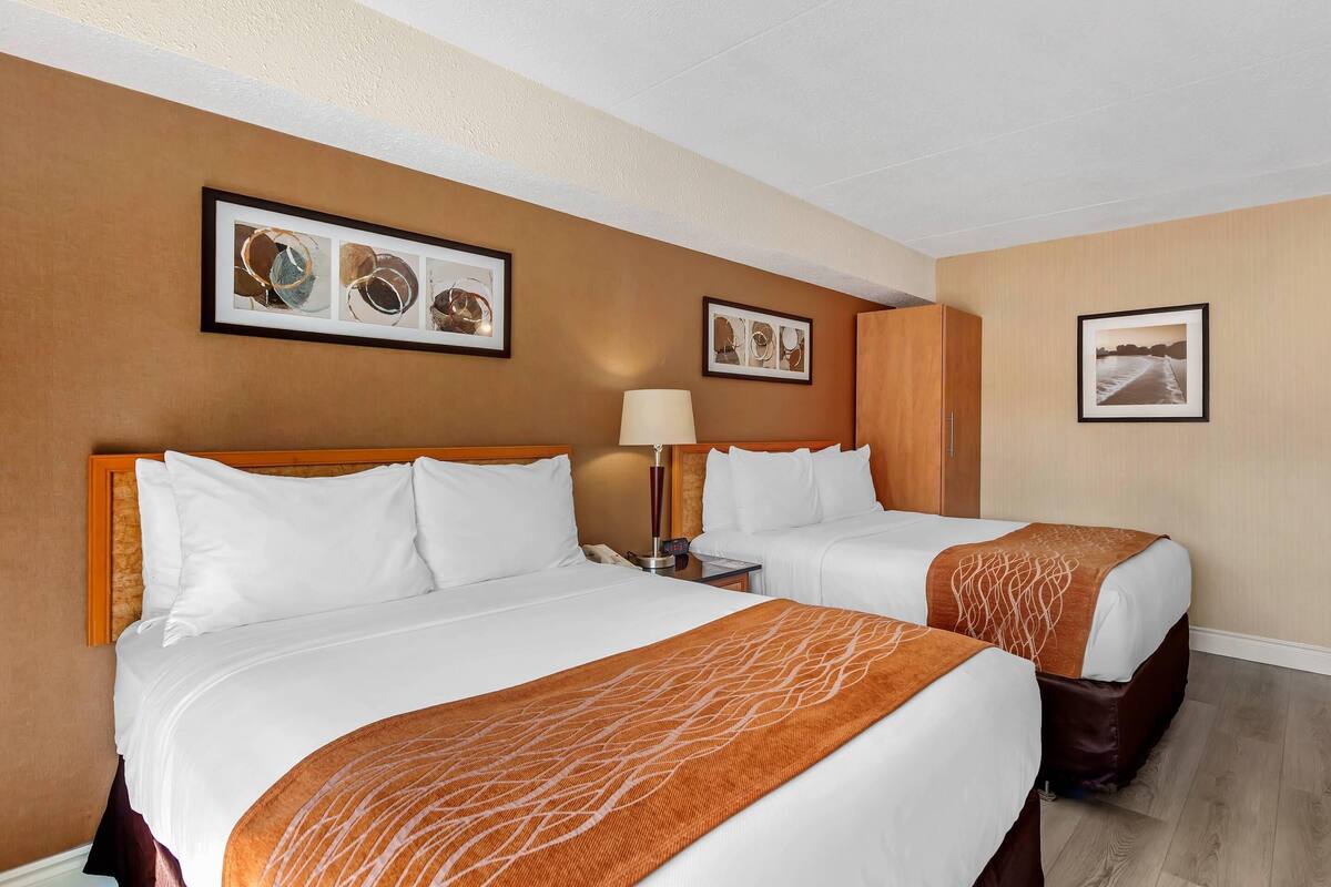 A hotel room with two beds, a nightstand with a lamp, and framed artwork on the walls.