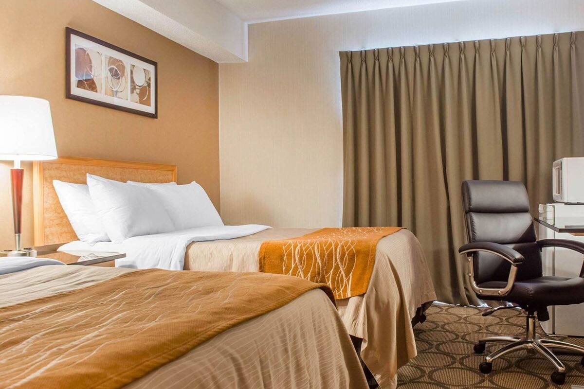 A hotel room with two beds, a desk with a chair, a lamp, and a picture on the wall.
