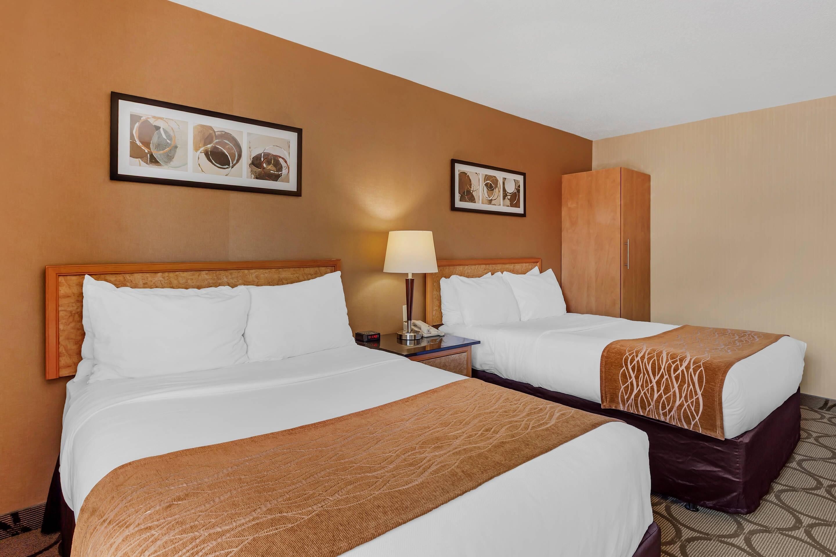 A hotel room with two beds, a nightstand with a lamp, and artwork on the walls.
