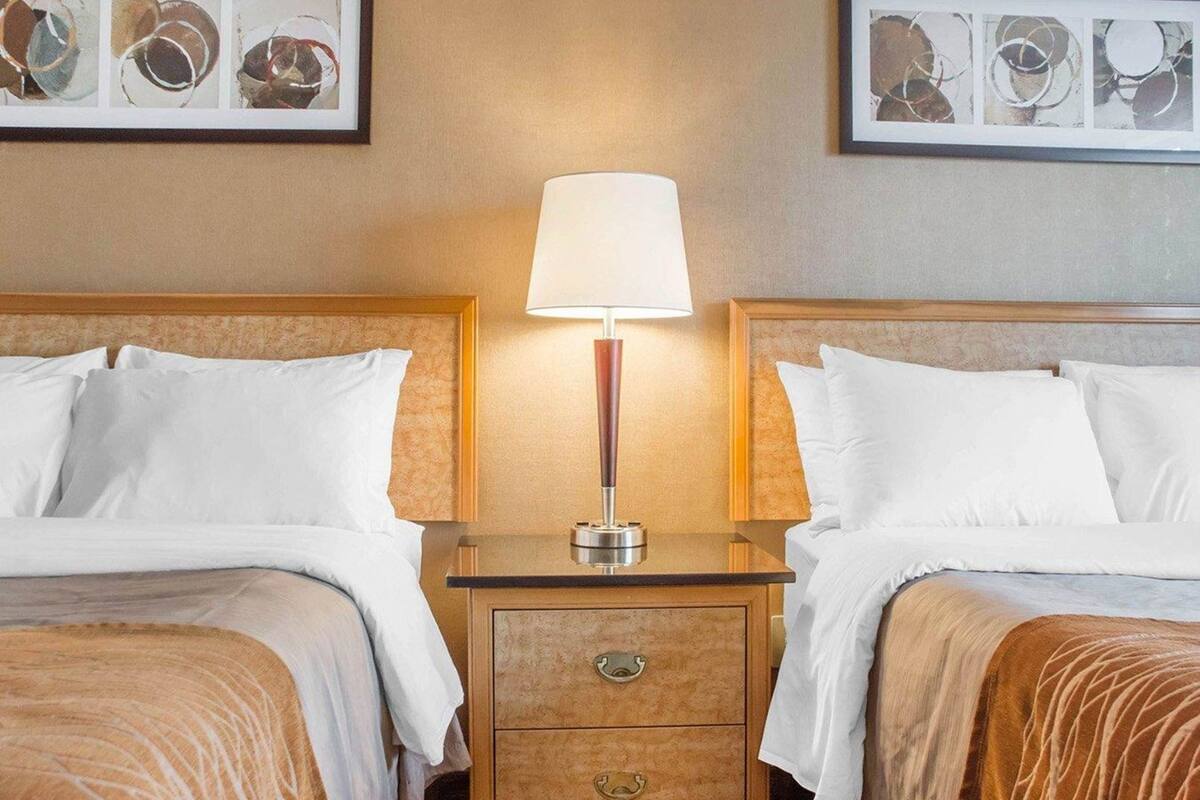 A hotel room with two beds, a nightstand with a lamp, and framed artwork on the walls.