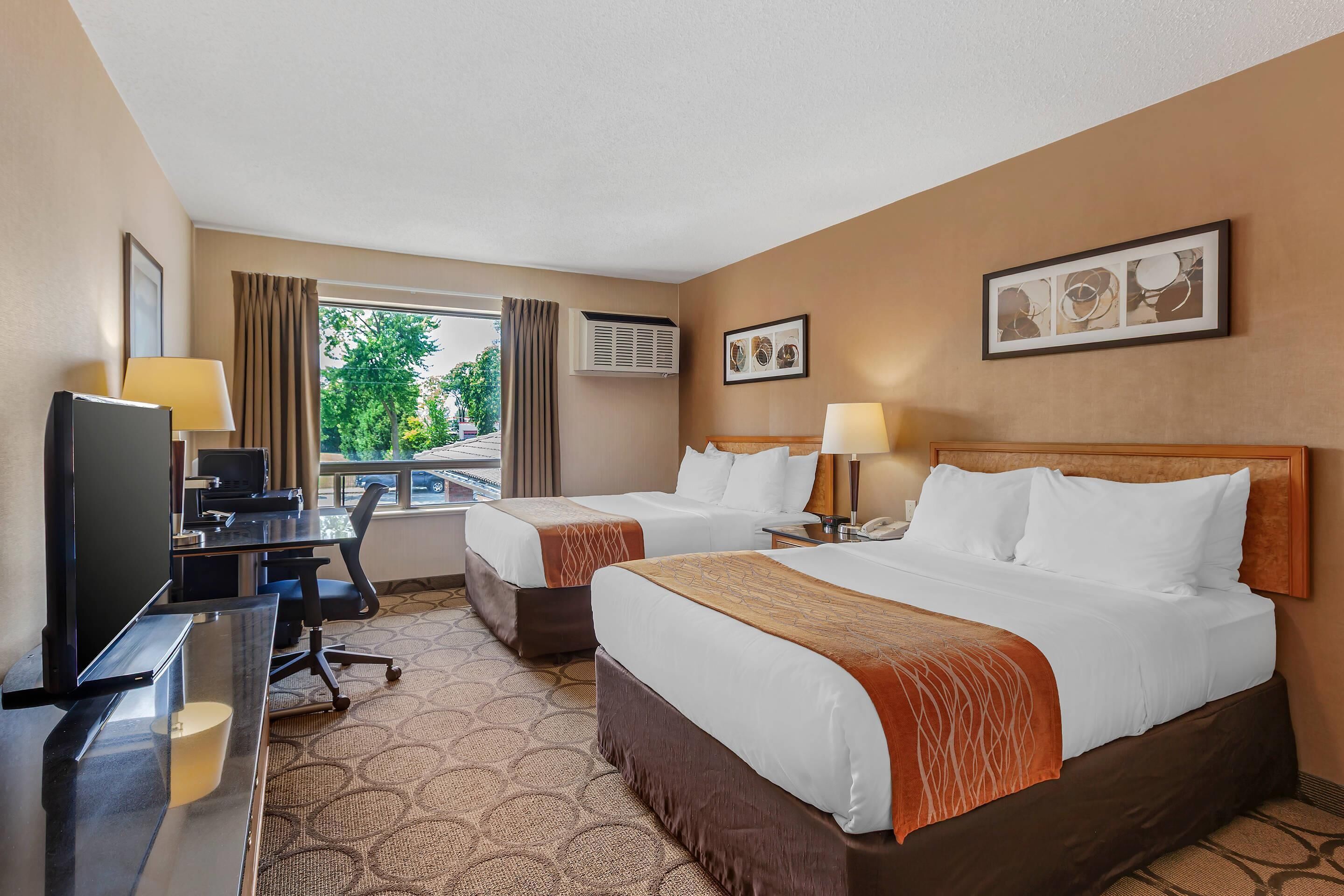 A hotel room with two beds, a desk, a TV, and a window with curtains.