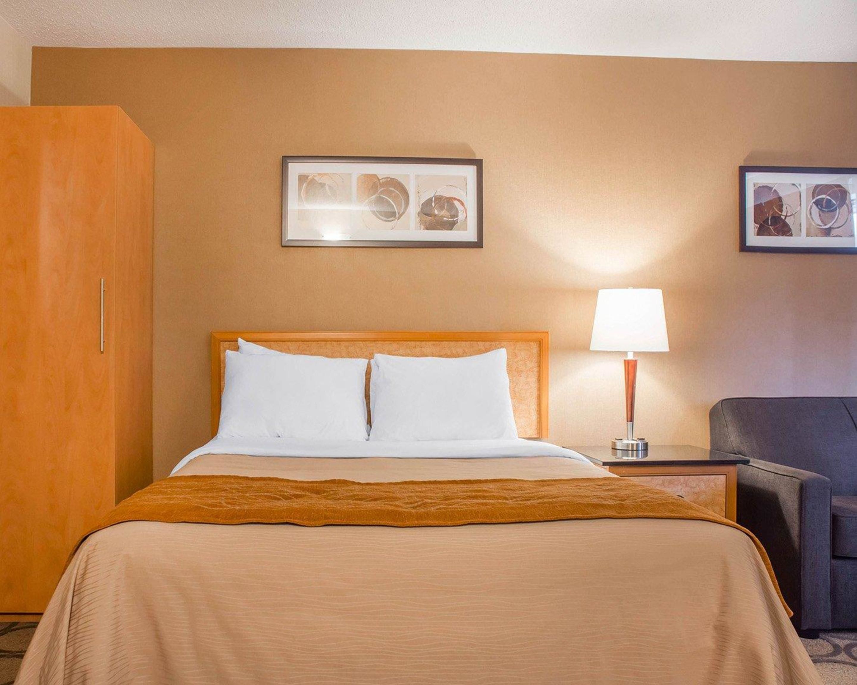 A hotel room with a bed, a nightstand, a lamp, a chair, and a wardrobe.
