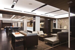 Un moderno vestíbulo de hotel con una zona de bar, asientos y un mostrador de recepción.