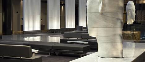 A modern lobby with a large white sculpture, seating areas, and a reflective floor.