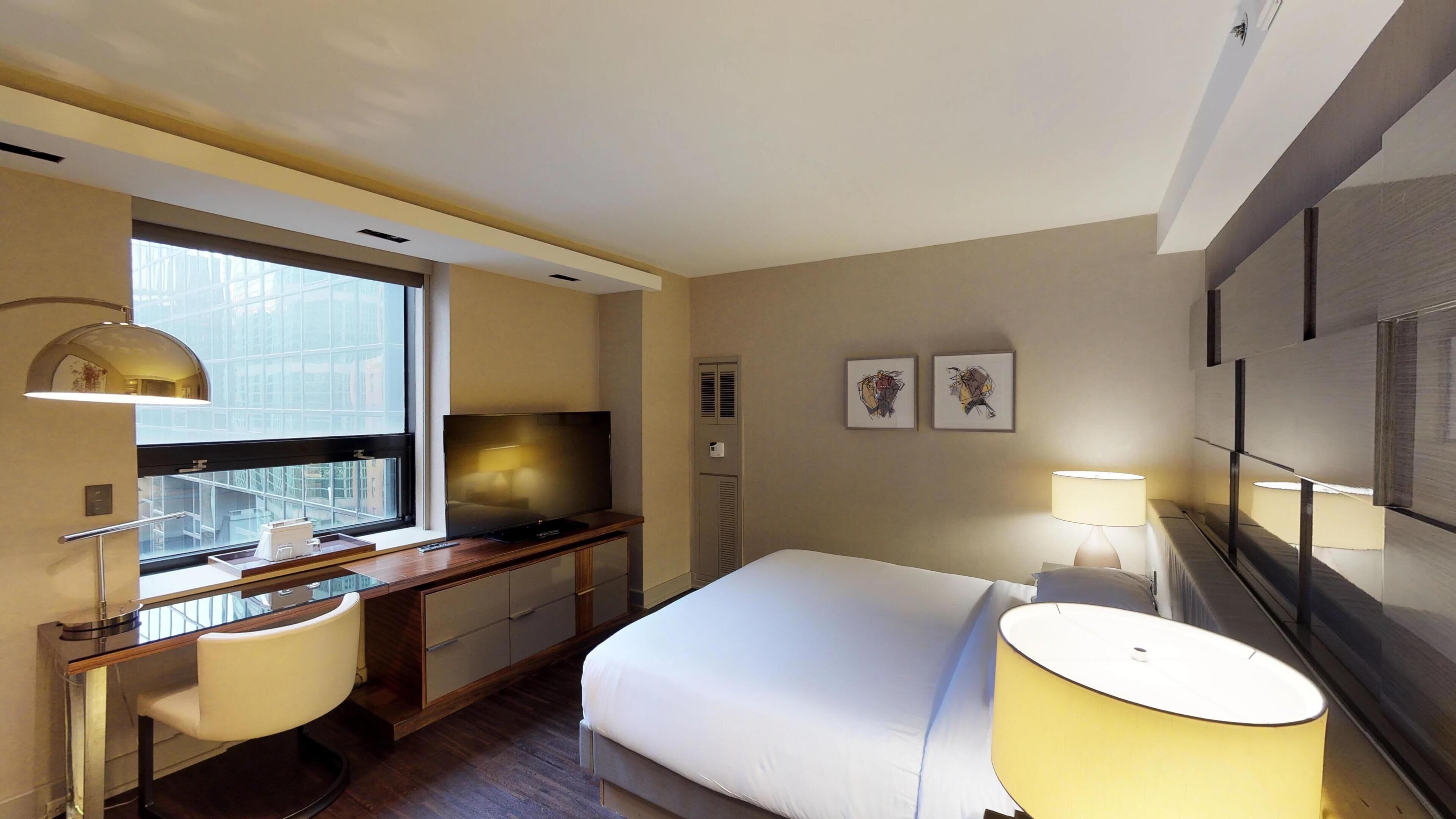 Een hotelkamer met een bed, bureau, stoel, televisie en kunst aan de muur.