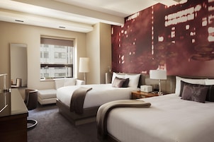 A hotel room with two beds, a desk, a chair, a window, and a large wall mural.