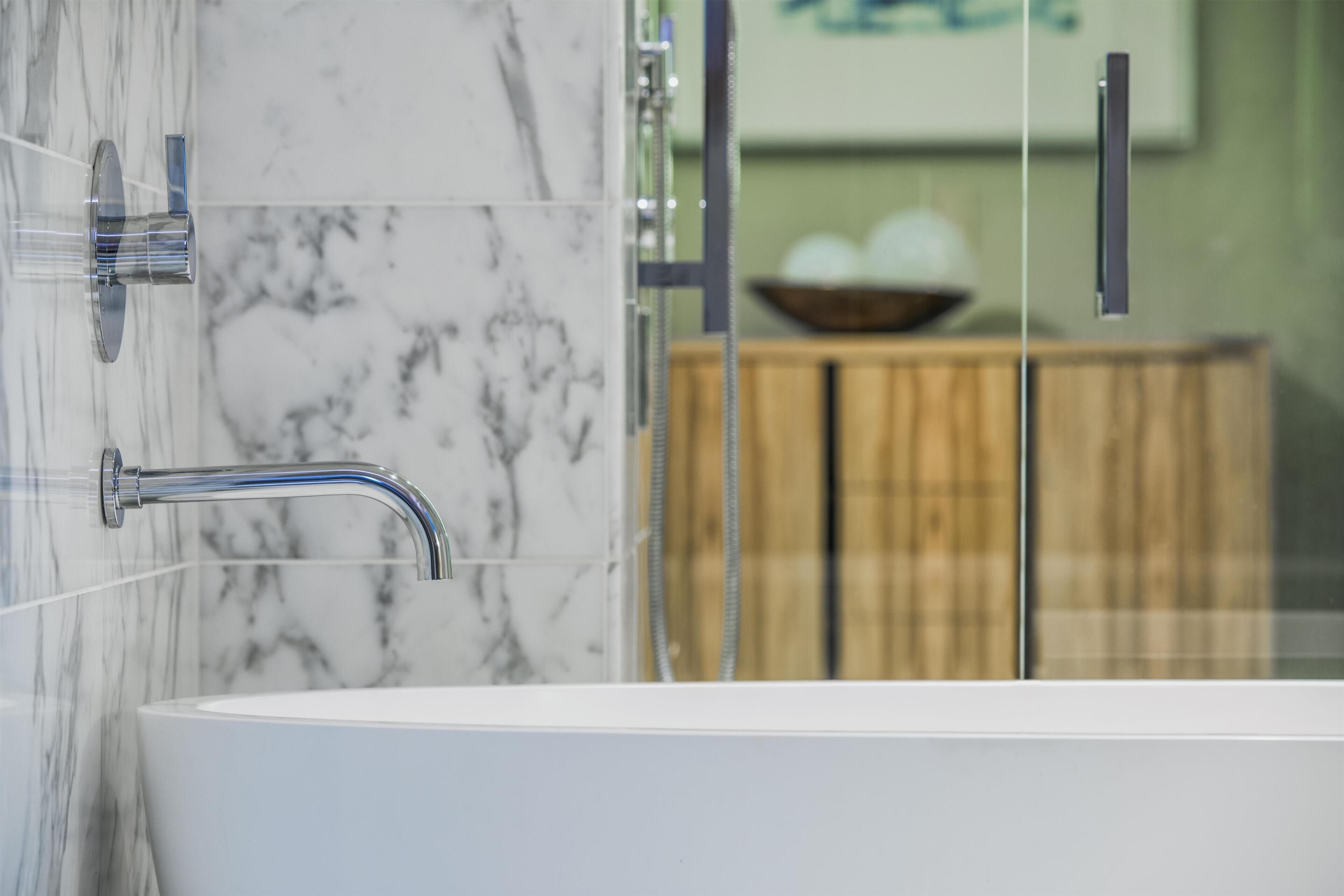 A bathroom with a marble wall, a bathtub, and a wooden cabinet in the background.