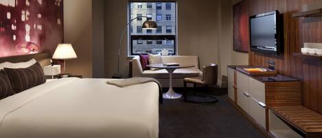 A hotel room with a large bed, a desk, a chair, a television, and a window with a city view.