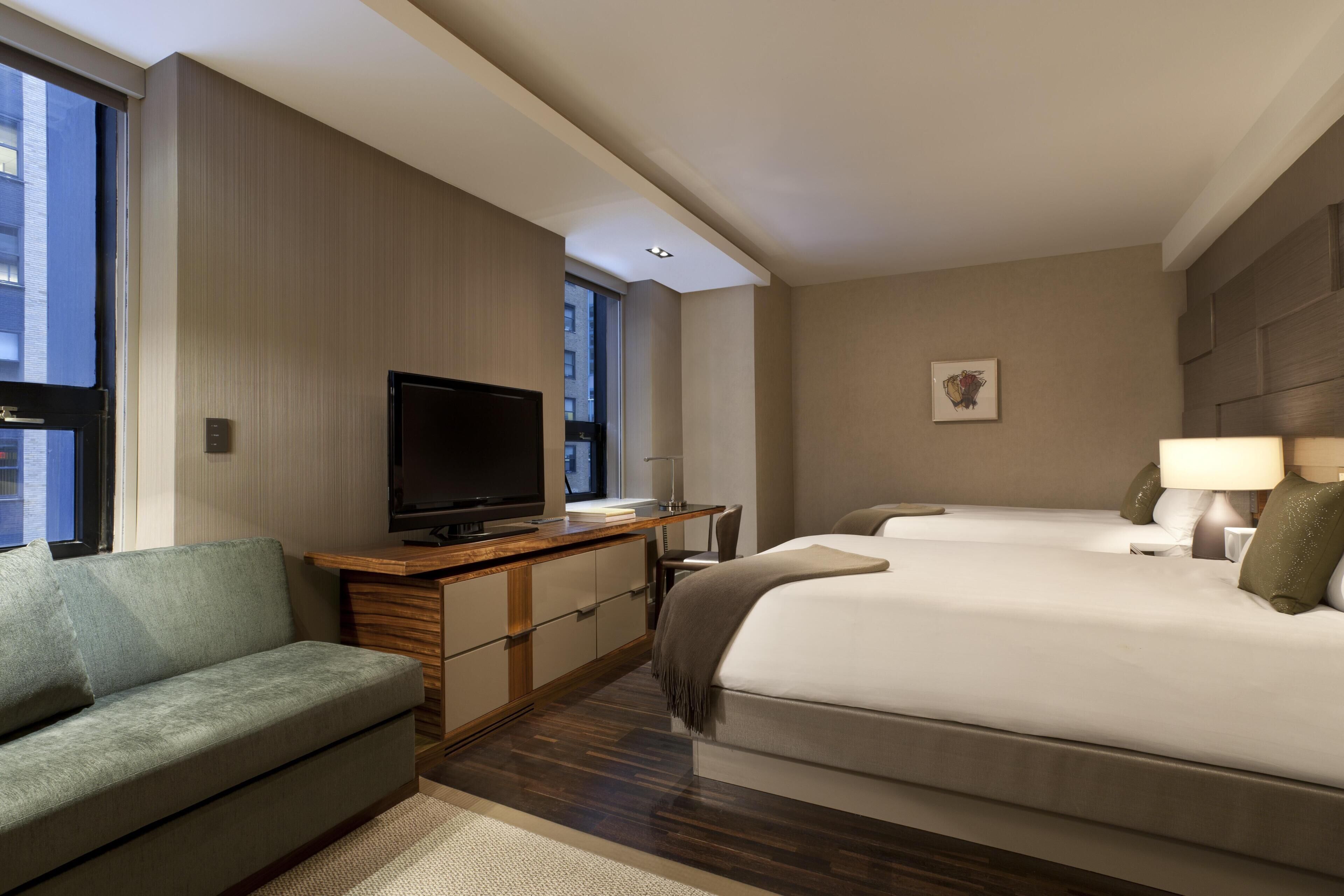 A hotel room with a sofa, a TV, a desk, a bed, and a nightstand.