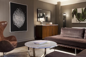 A modern living room with a sofa, a round coffee table, and a chair. There are artworks on the walls and a cabinet with a mirror. - Hyatt Grand Central New York (New York)