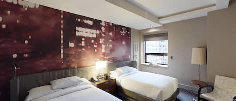 Habitación de hotel con dos camas, un mural grande en la pared, una ventana con vistas a edificios, una mesita de noche con lámpara y una silla.
