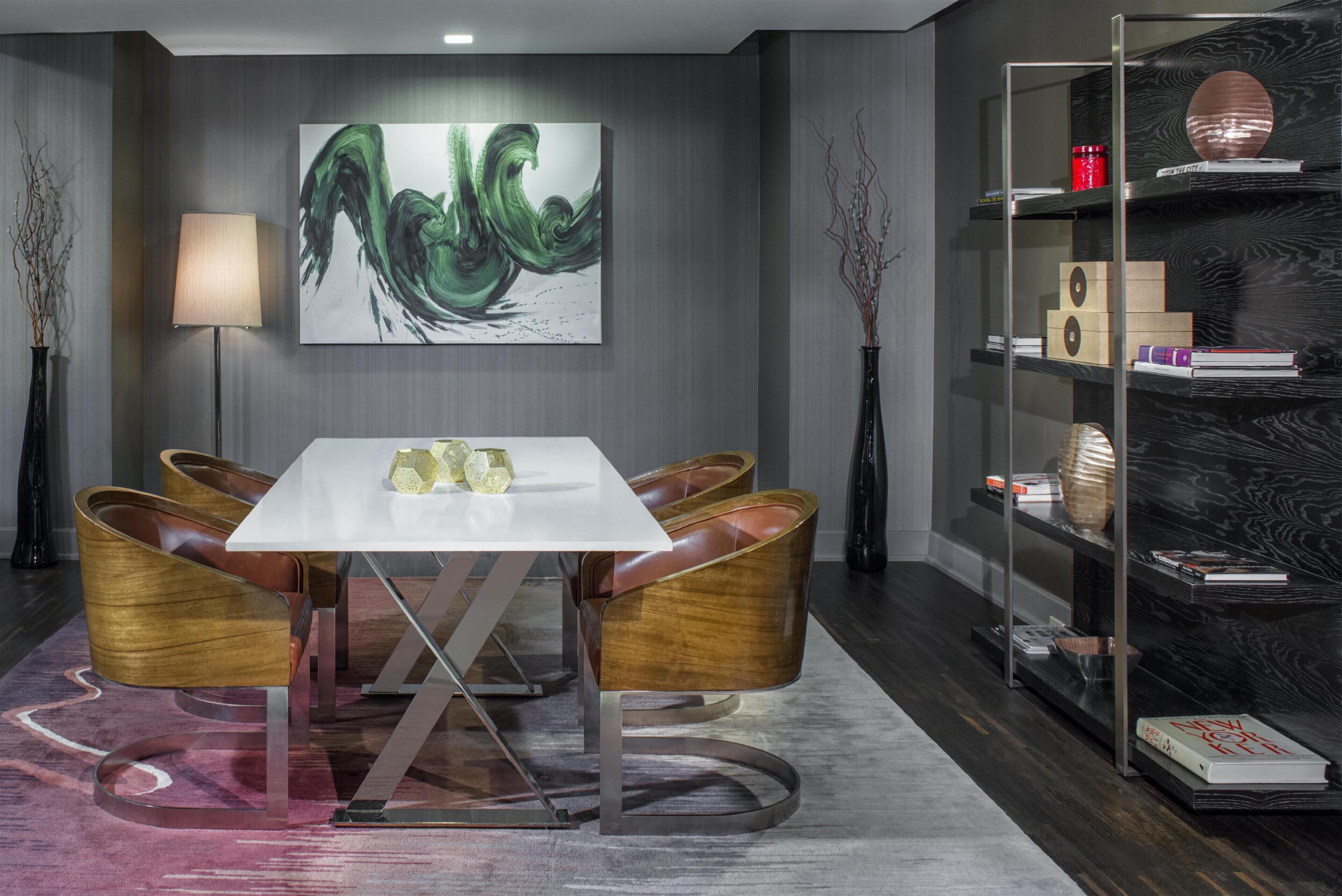 A modern dining area with a white table, leather chairs, a large abstract painting, and a bookshelf with books and decorative items.