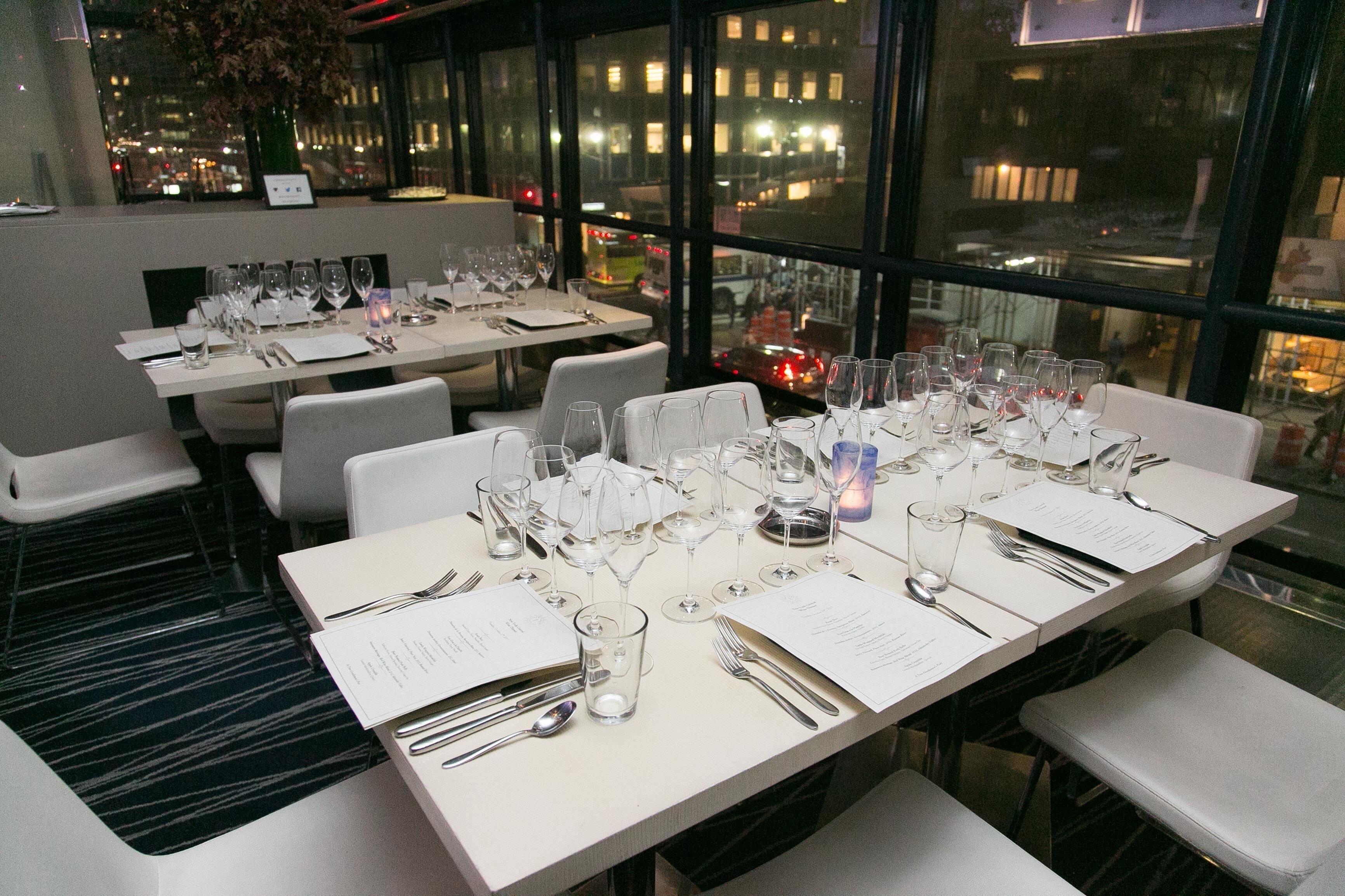 Un restaurante con varias mesas dispuestas para comer, cada una con carta, cubiertos y copas de vino.