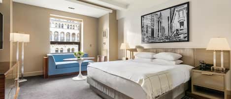 Een hotelkamer met een groot bed, een blauwe bank, een kleine tafel met een vaas en een schilderij aan de muur.