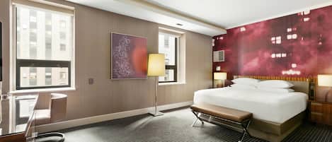 A hotel room with a large bed, a desk, a chair, a window, and a wall with a red abstract painting.