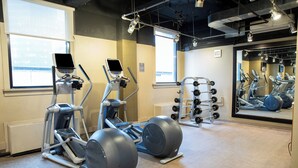 A gym with exercise equipment, a weight rack, and large windows. - Hyatt Grand Central New York (New York)