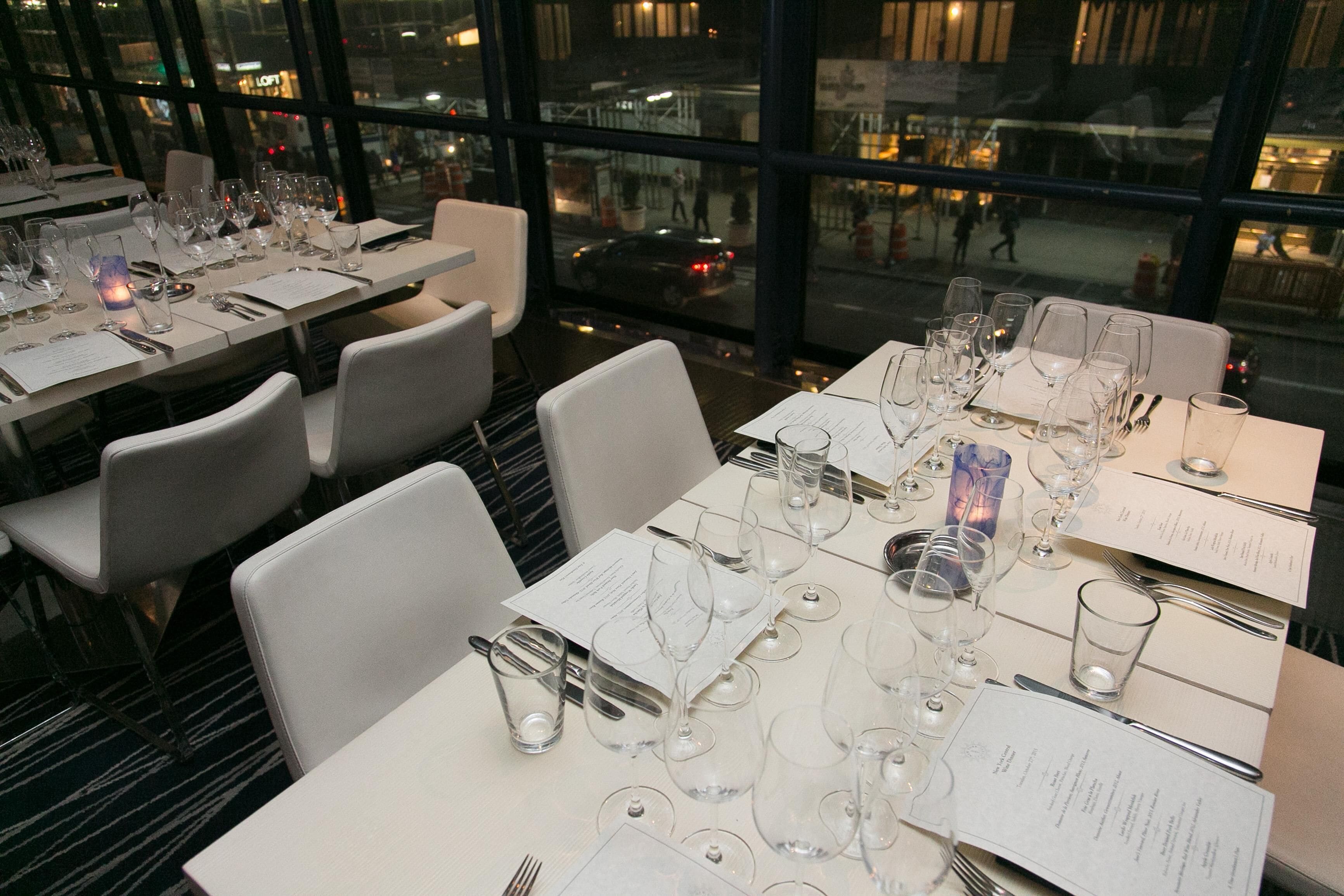 A restaurant with tables set for dining, chairs, and a view of the street through large windows.