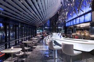 Een moderne bar met een gebogen toonbank, verschillende zithoeken en een uitzicht op de stad door grote ramen.