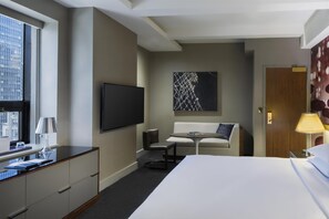 Habitación de hotel con cama, escritorio, silla, televisor y un cuadro en la pared.
