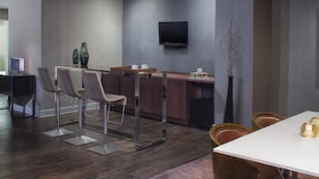 Habitación de hotel moderna con área de comedor, televisor de pantalla plana en la pared y un cuadro abstracto grande.
