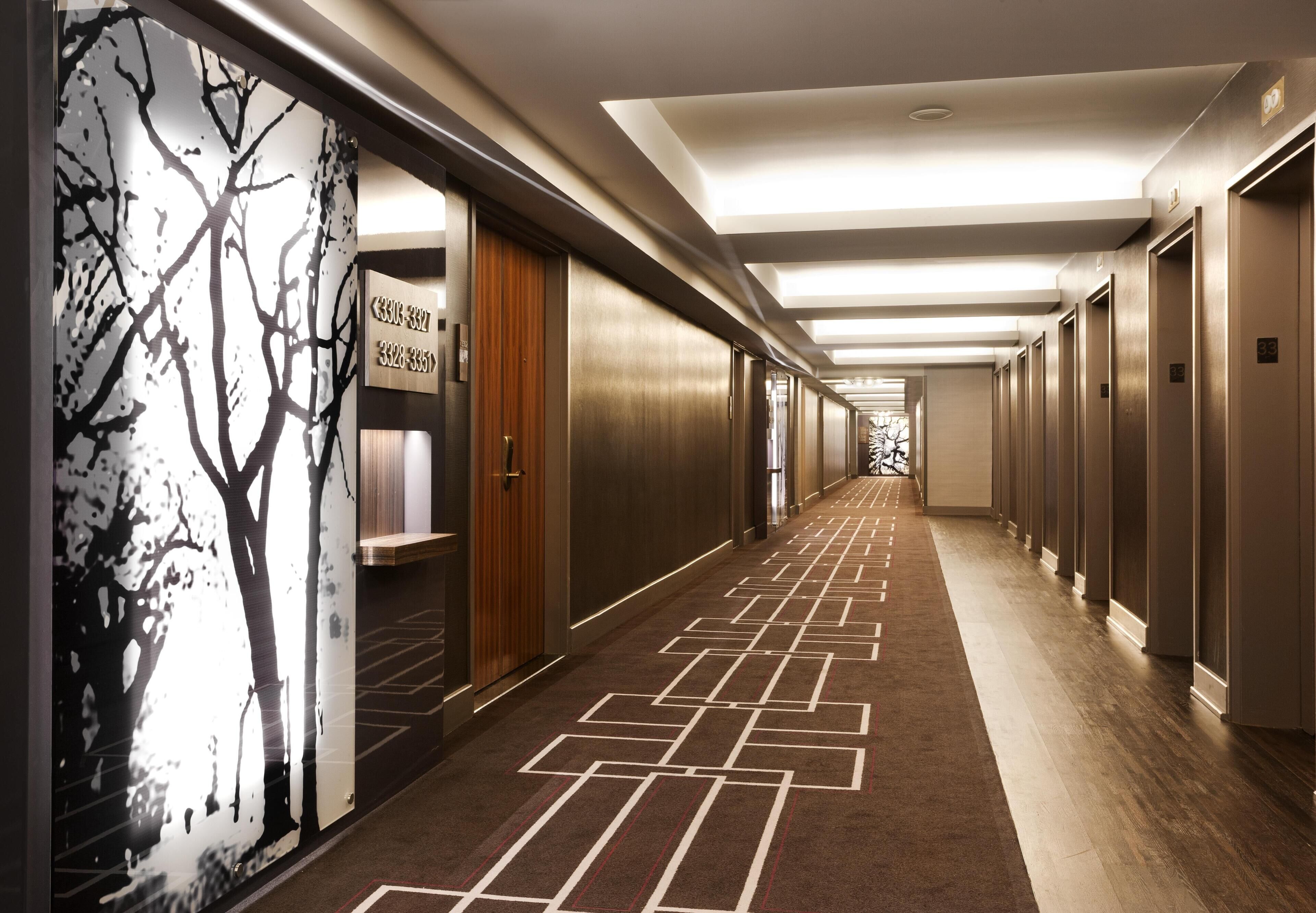 A hotel hallway with a patterned carpet, wooden doors, and a ceiling with recessed lighting.
