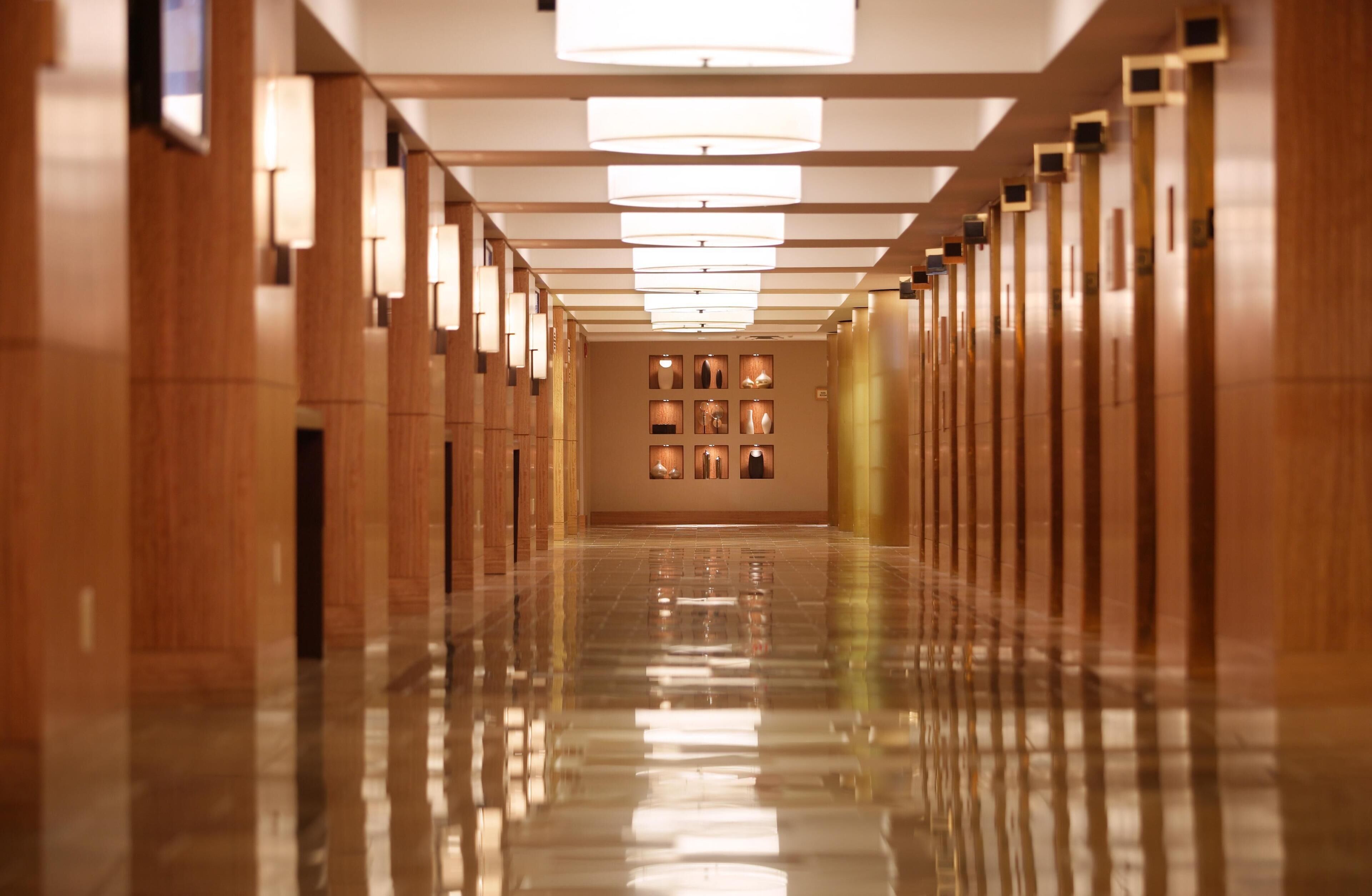 A long, polished hallway with wooden paneling and a series of wall-mounted lights.