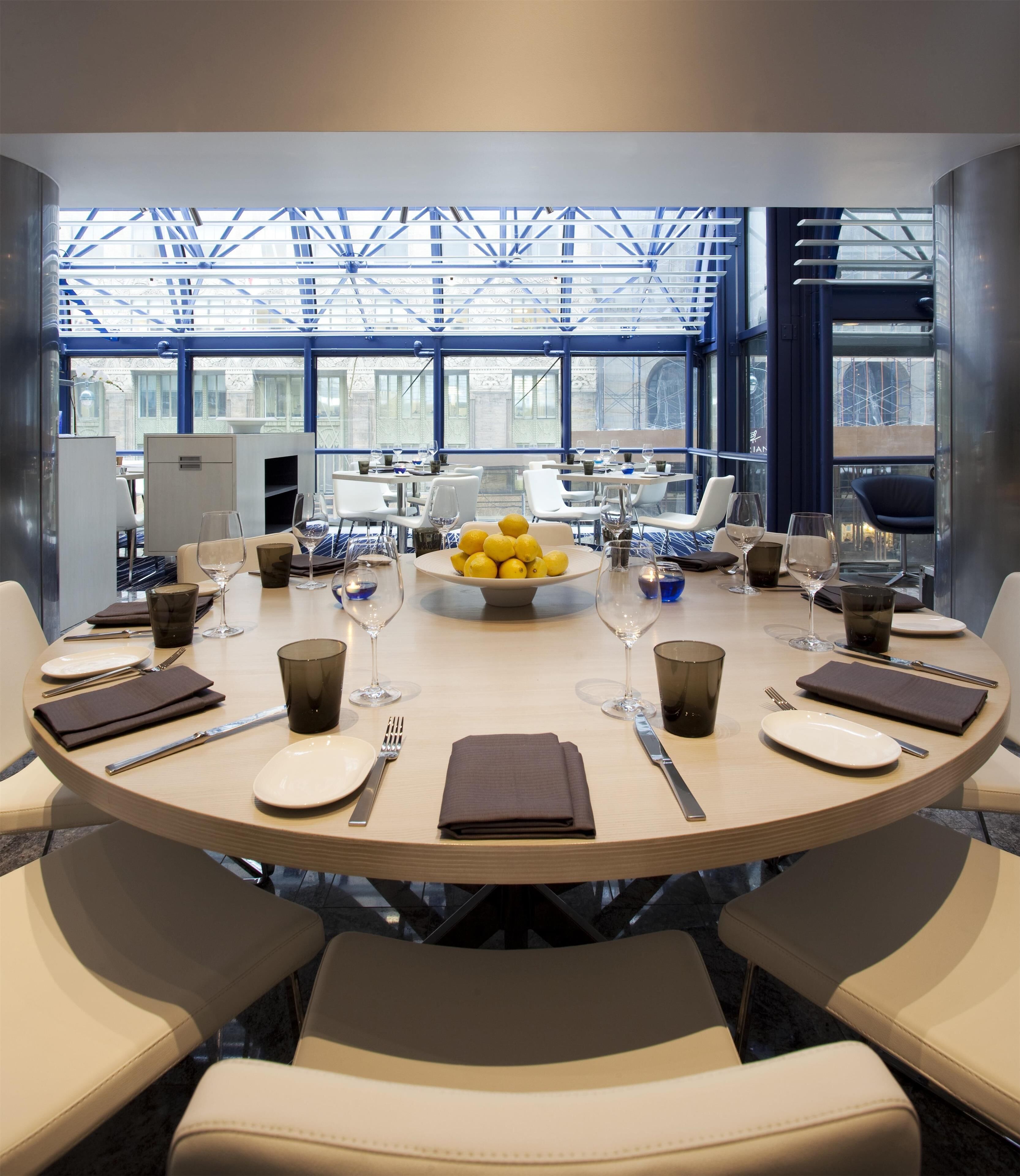 A modern dining area with a round table set for six, surrounded by chairs, with a large window providing a view of the cityscape.