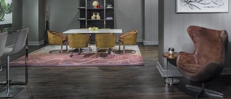 Un comedor moderno con una mesa blanca, cuatro sillas, un tapete estampado y un sillón marrón.